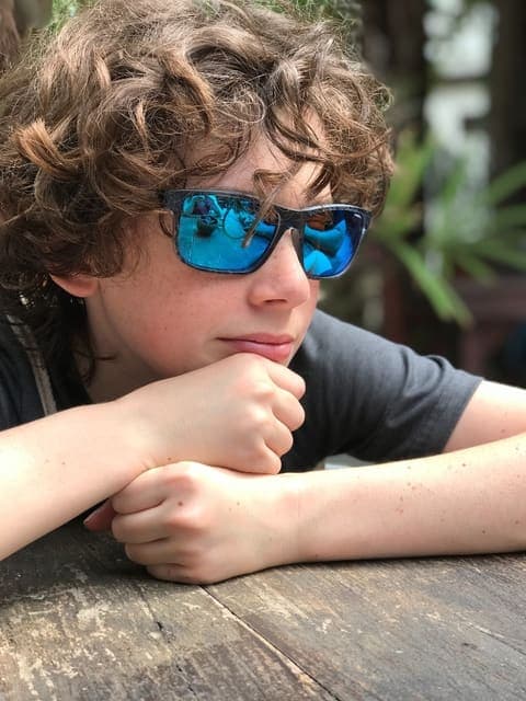 Photo of a boy resting his chin on his hands at a wooden table