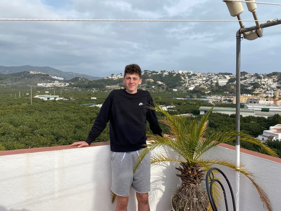 Photo of a man leaning on a rooftop terrace wall in Spain, hills and town behind
