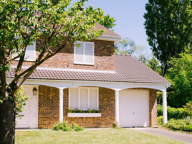 Photo of a brick house behind a tree on a summer afternoon