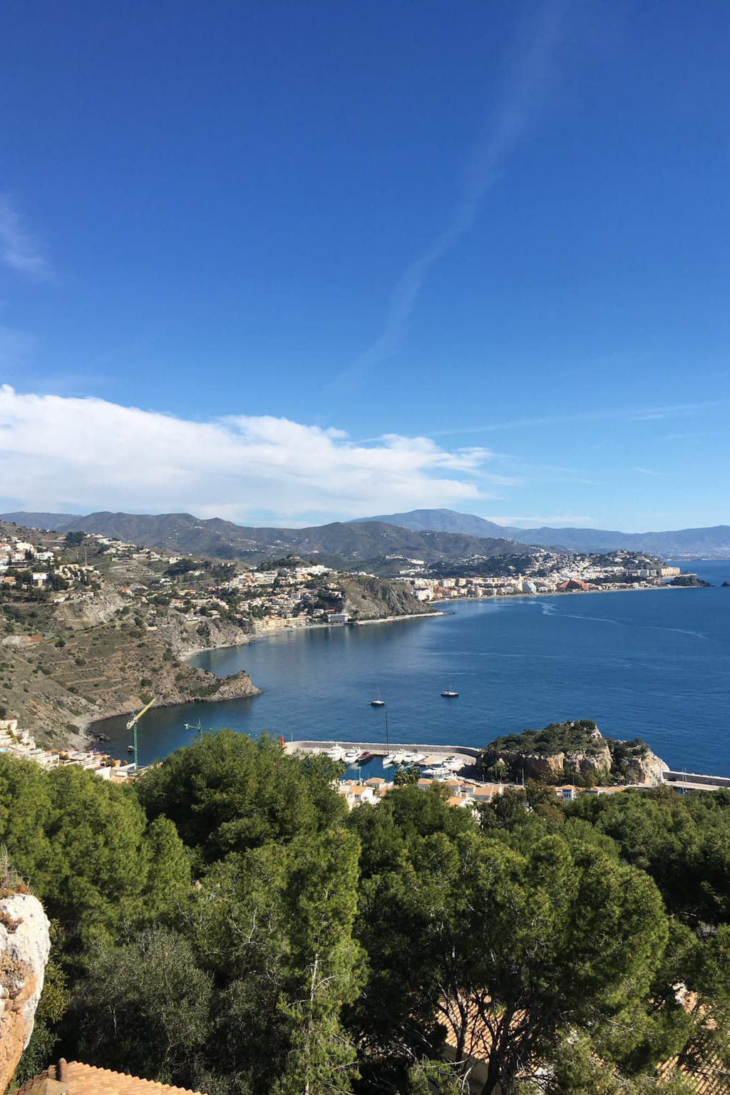 Photograph of a Mediterranean bay with a harbour, headland and hills behind