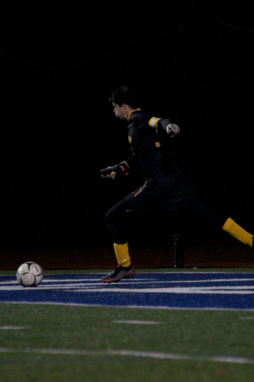 Photo of a goalkeeper kicking a ball on a floodlit pitch at night