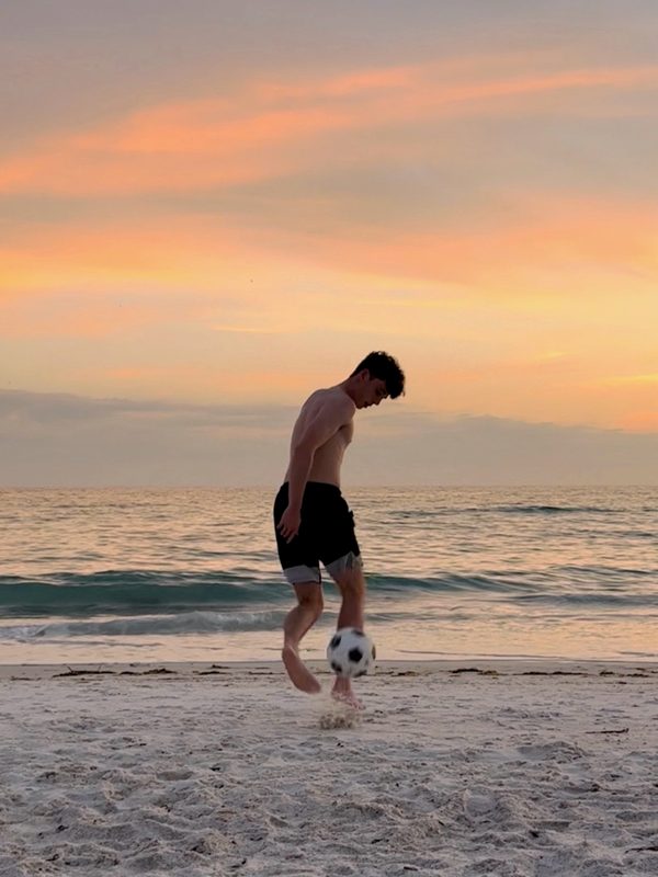 Photo of a young man juggling a football on a beach at sunset